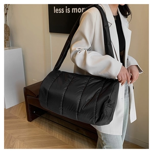 Detail of black quilted puffer cylinder bag featuring wide padded shoulder strap