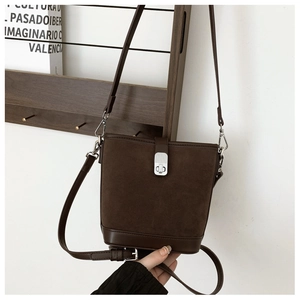 Detail of dark brown bucket bag with matte suede texture and silver metal lock closure