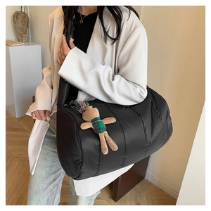 Detail of black quilted down shoulder bag with a plush bunny charm on wide strap