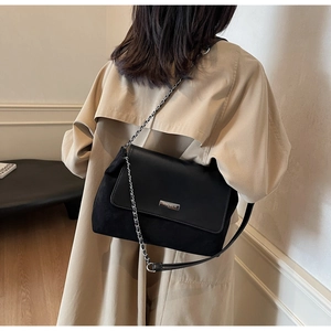 Detail einer Vintage-Schultertasche in Schwarz mit Silberkette getragen zu einem beigen Mantel
