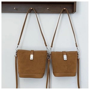 Detail view of two brown suede bucket bags in large and small sizes on wooden hooks