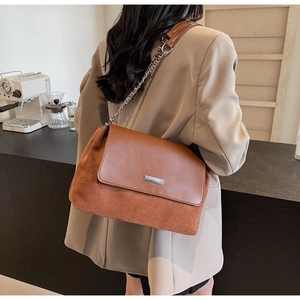 Detailansicht einer braunen Vintage-Umhängetasche aus Leder mit Kettenriemen am Tisch