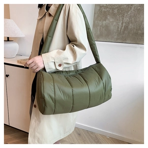 Side view of olive green quilted puffer bag with wide strap on a model shoulder