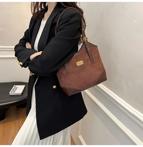 Detailansicht der dunkelbraunen Wildleder-Tragetasche mit Metallplakette und Riemen