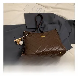 Détail du sac seau matelassé marron avec finitions dorées et breloque baseball sur veste