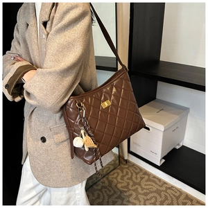 Gros plan sur le sac seau matelassé marron foncé avec fermoir doré et breloque baseball