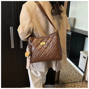 Détail d'un sac bandoulière matelassé marron avec fermoir tournant doré et pendentif