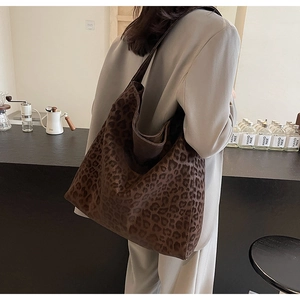 Side view of a large leopard print tote bag worn on shoulder in a cozy cafe setting