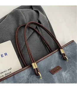 Detail of canvas tote bag with brown leather handles and gold metal ring hardware