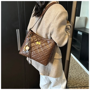Détail d'un sac hobo matelassé marron avec fermoir doré et pendentif de baseball