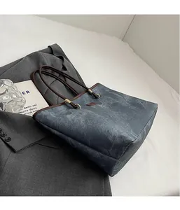 Detailed view of a grey-blue tote bag with brown leather handles on a grey blazer