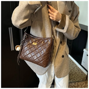 Détail d'un sac seau matelassé marron avec fermoir doré et pendentif de balle de baseball