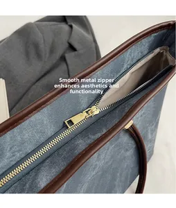 Detail of a smooth golden hardware zipper on a denim tote bag with brown leather trim