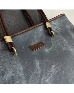 Detail of grey twill fabric tote with brown leather trim and golden metal rings