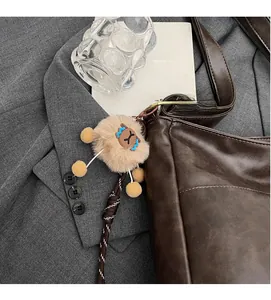 Close-up of a plush bear charm with woven strap on a brown leather tote bag