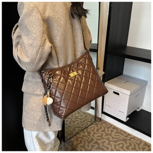 Détail d'un sac seau matelassé marron avec fermoir doré et breloque de baseball