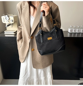 Detailansicht der schwarzen Retro-Tasche mit Wildledertextur und goldener Plakette