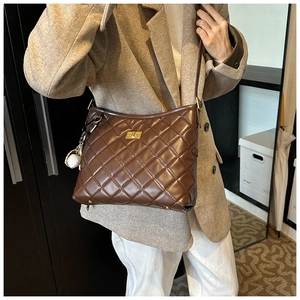 Détail d'un sac seau matelassé marron foncé avec fermoir doré et charme porté par mannequin