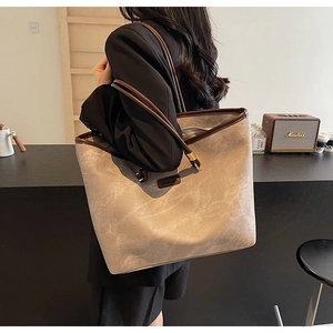 Detail of a large gray tote bag with contrast brown leather handles on a model's shoulder
