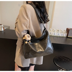Detail of vintage black leather tote bag with a plush charm on model in cafe setting