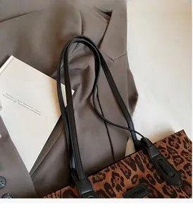 Detail of leopard print tote bag with black leather handle on a grey blazer