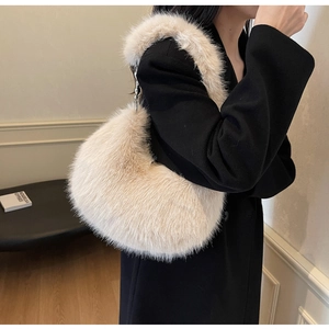 Gros plan d'un sac hobo en fausse fourrure crème porté sur un manteau noir chic