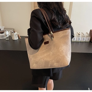 Detail of a large beige marble-textured tote bag with brown straps in a cafe setting