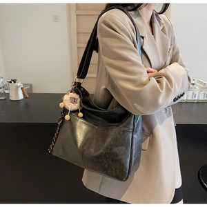 Detail of matte black tote bag with vertical stitching and wide strap on model