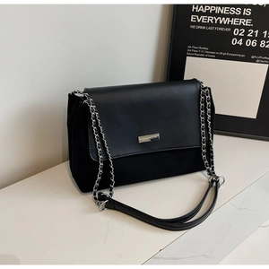 Detail der schwarzen Schultertasche aus Wildleder mit silberner Metallplakette und Kette