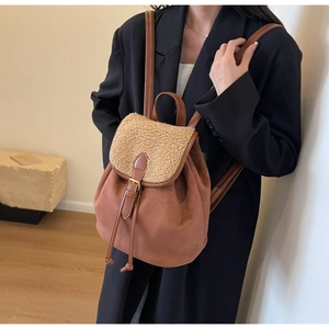 Detail of a brown suede backpack featuring cream faux shearling trim and buckle straps