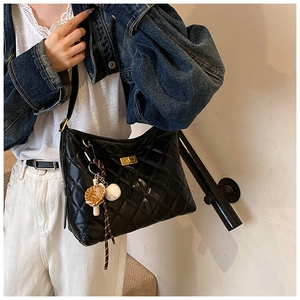 Sac à bandoulière matelassé noir avec fermoir doré et breloque porté par mannequin