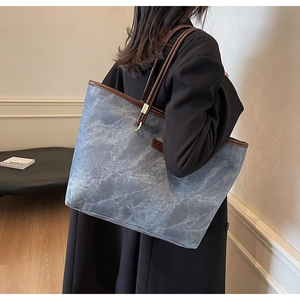 Detail of large tote bag with blue marble texture and brown leather straps on shoulder