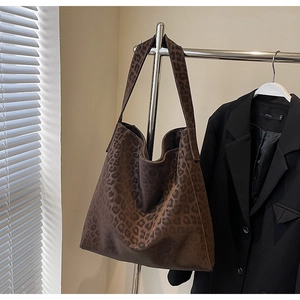 Detail of a large leopard print tote bag in soft suede-like fabric hanging on a rack