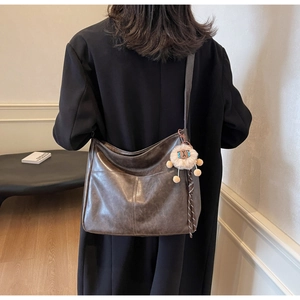 Detail view of a vintage dark brown messenger bag with a soft plush sheep charm accessory