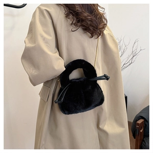 Detail of black faux fur bucket bag with gold chain strap on khaki trench coat