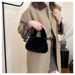 Model showcasing a plush black faux fur bucket bag with a gold chain strap indoors