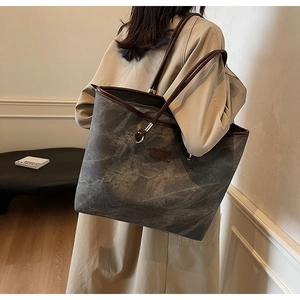 Detail view of large grey tote bag with marble texture and brown leather handles on shoulder