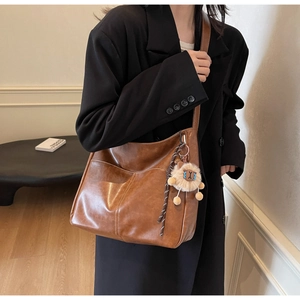 Brown vintage hobo bag with plush lion charm shown on a black oversized winter coat