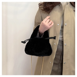Detail of a black plush bucket bag with golden chain strap held by a model in a trench coat
