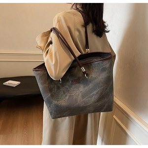 Detail of dark grey marble tote bag with brown leather handles worn with a beige coat