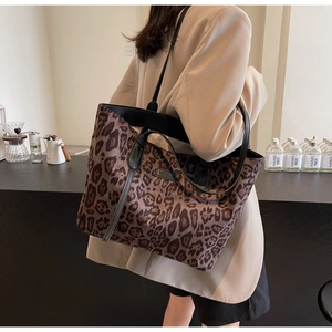 Detail of leopard print tote bag with black leather straps and woven label on side