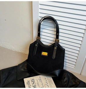 Detail der schwarzen matten Wildleder-Einkaufstasche mit Goldplakette auf einer Lederjacke