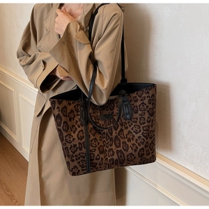 Detailed side view of leopard print tote bag with black leather handles and logo plate