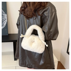 Close-up of white faux fur handbag with gold chain strap on a brown leather jacket