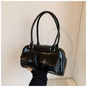 Détail d'un sac à main noir en cuir verni brillant avec deux poches avant et fines poignées