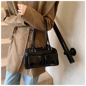 Détail d'un sac à bandoulière noir brillant avec poches avant sur un manteau beige