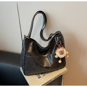 Macro shot of black vintage PU leather tote bag with a brown plush bear keychain charm