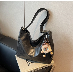 Close-up of black retro hobo bag with oil wax leather texture and plush lion pendant