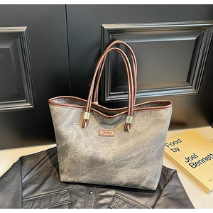 Detail of grey textured tote bag with brown leather handles and a fashion brand tag