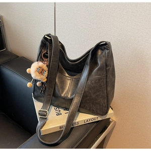 Detail of grey retro leather tote bag featuring a front pocket and plush lion charm
